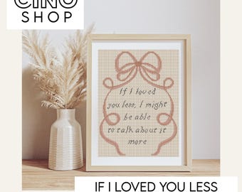 May include: A framed cross-stitch pattern with the text "If I loved you less, I might be able to talk about it more." The design features a bow and decorative border in a soft pink hue. The frame is a light wood colour.
