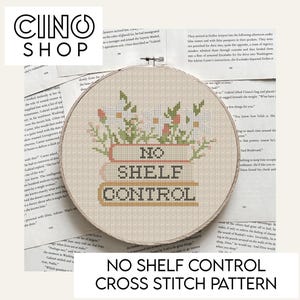 May include: A cross stitch pattern for a hoop with the text "No Shelf Control" in a brown, orange, and white color scheme. The hoop is surrounded by a floral design with pink, white, and green flowers.