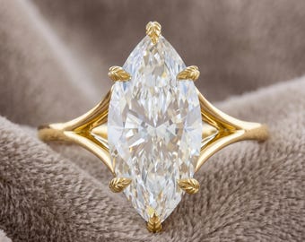 May include: A gold ring featuring a large, marquise-cut clear gemstone held by six prongs shaped like small leaves. The band has a split-shank design that tapers toward the center setting, showcasing a polished yellow gold finish throughout.
