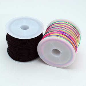 May include: Two white plastic spools of cord. One spool is wrapped with solid black cord, while the other spool features a vibrant, multi-coloured cord with repeating stripes of neon pink, yellow, green, blue, and orange throughout the length.