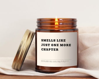 May include: A brown glass candle jar with a gold lid. The candle is lit and the jar has a white label with the text "Smells like just one more chapter".