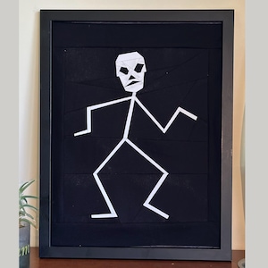 May include: Framed artwork with a white geometric figure on a black backdrop. The figure is a stick person with a geometric head and limbs. The artwork is in a black frame, offering a modern, minimalist aesthetic. The frame is approximately 30 cm x 40 cm.