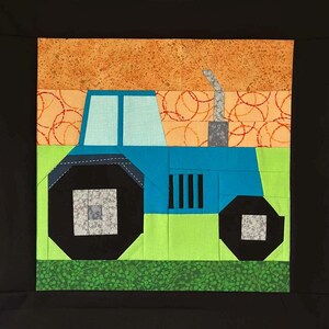 May include: A quilted square featuring a blue tractor with black wheels and a gray smokestack. The tractor is set against a green field and an orange sky with a circular pattern. The quilt is framed by a black border.