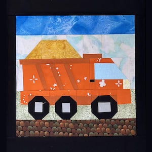May include: A colorful quilt square featuring an orange dump truck with black wheels and a yellow load. The truck has a light blue window and is set against a sky of blue and white. The base of the truck rests on a brown and green surface.