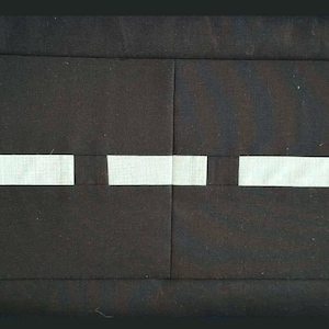 May include: A rectangular, black fabric item with three white rectangular accents. The item has a stitched border and is likely a placemat or decorative piece. The white accents are evenly spaced.
