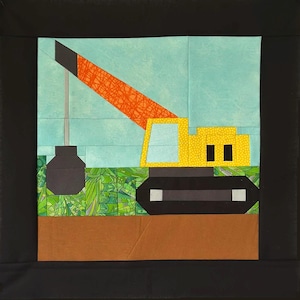 May include: A colorful quilt block featuring a yellow crane with a black base and an orange boom. The crane is set against a light blue sky and a green and brown landscape. The block is framed in black.