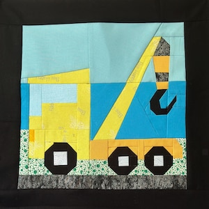 May include: A colorful, handmade quilt block featuring a yellow crane truck against a blue sky. The crane has a black hook and wheels, with a green and white dotted border at the bottom. The words "Bee Happy" are printed on the crane.