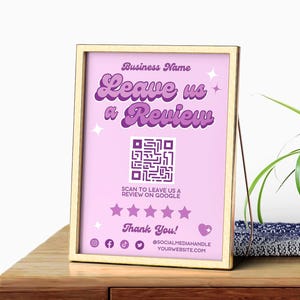 Pode incluir: Uma placa emoldurada com fundo roxo claro e moldura dourada. A placa diz "Leave us a Review" em texto roxo, com um código QR e o texto "Scan to leave us a review on Google". Ícones de mídia social também estão incluídos.