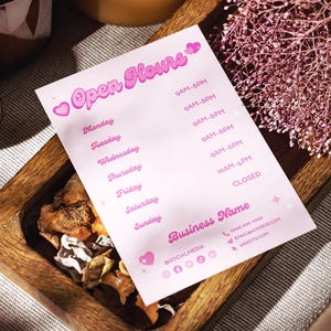 May include: A pink and white sign with the text "Open Hours" in pink cursive lettering. The sign lists the business hours for each day of the week, with the hours listed in AM and PM. The sign also includes the business name, social media icons, and contact information.