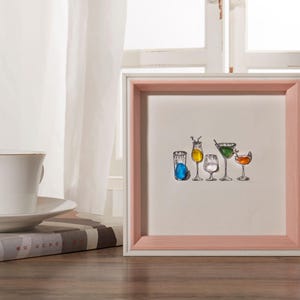Op de afbeelding: Een wit fotolijstje met een roze passe-partout en een witte rand. Het lijstje bevat een zwart-witte tekening van zes verschillende glazen met drankjes. De glazen zijn gevuld met verschillende gekleurde vloeistoffen en garnituren.