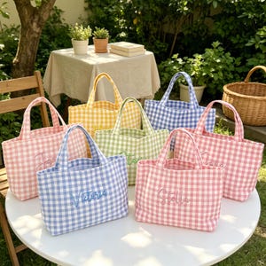 Peut inclure: Une collection de six petits sacs fourre-tout avec un motif à carreaux vichy dans diverses couleurs pastel, notamment rose, bleu, jaune et vert. Chaque sac possède deux anses et est brodé d'un prénom unique en écriture cursive sur le devant.