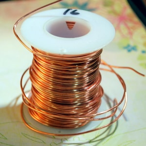 May include: A spool of copper wire, wound tightly on a white plastic spool. The spool is labeled with the number "16".