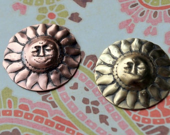 May include: Two metal sun-shaped ornaments with a face on each. One is copper and the other is gold.
