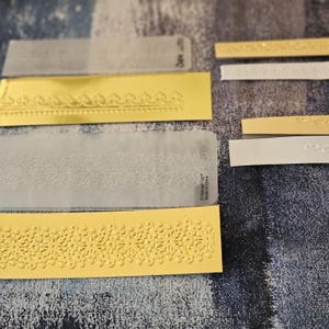 May include: A set of six gold and white embossed paper strips with a decorative lace pattern. The strips are made by Stampin' Up! and are made in China.