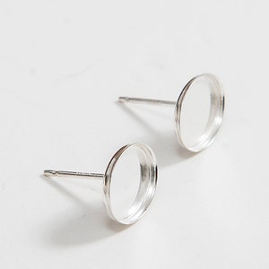 May include: A pair of silver earring settings with round bezels. The bezels are empty and ready to be filled with a cabochon.