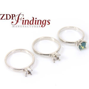 Könnte beinhalten: Drei silberne Ringfassungen mit Krappen zur Aufnahme von Edelsteinen. Die Ringfassungen befinden sich auf einer weißen Oberfläche.  ZDP Findings MANUFACTURER ist in roter Schrift oben im Bild gedruckt.