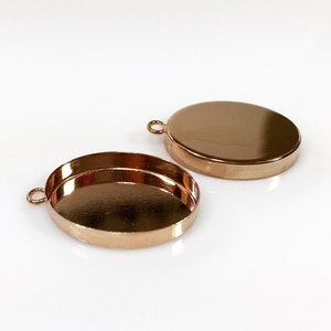 May include: Two gold-toned oval-shaped metal pendant trays with a loop at the top for attaching a chain or cord.
