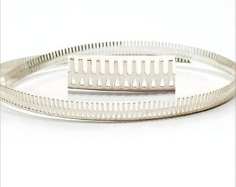 May include: A silver metal ring with a series of small, evenly spaced holes around the circumference. The ring is designed to be used as a cable organizer.