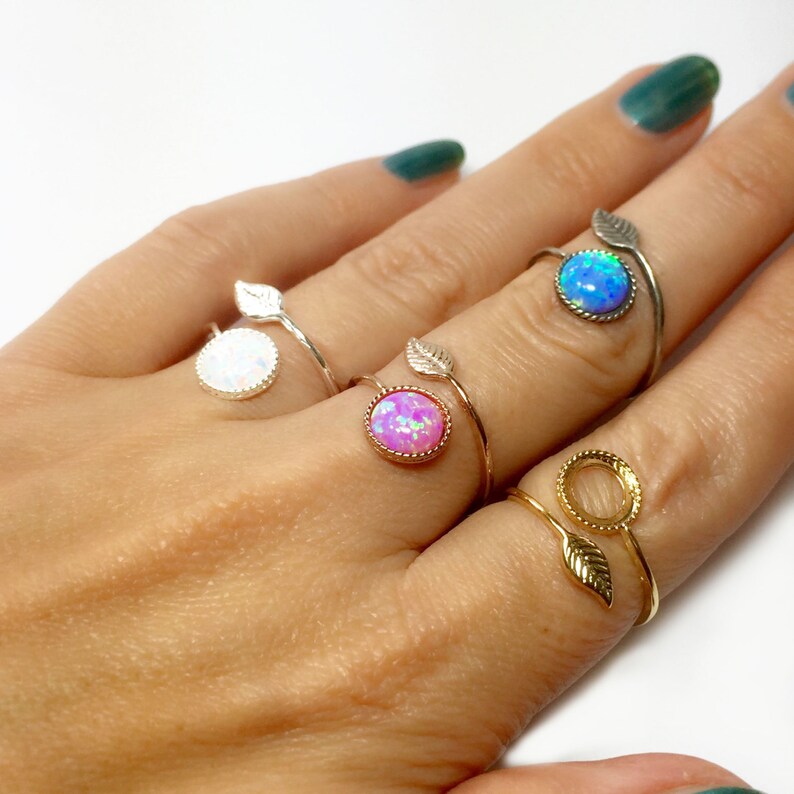May include: A hand model wearing four rings with opal stones. The rings are silver and gold with leaf accents. The opals are white, pink, blue, and clear.