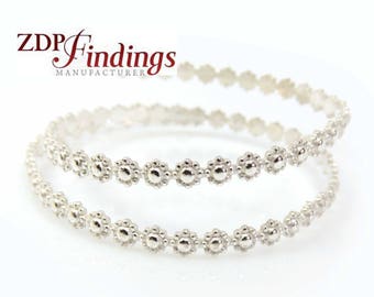 May include: Two silver bangle bracelets with a delicate floral design. Each bracelet is made of a series of small, connected circles that create a flower-like pattern.