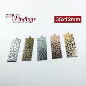 Może przedstawiać: Pięć prostokątnych metalowych zawieszek z fakturowaną powierzchnią. Zawieszki mają wymiary 35 mm x 12 mm i są dostępne w kolorze srebrnym, złotym, różowym złocie i dwóch odcieniach srebra.