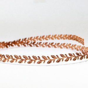May include: A copper-coloured headband with a delicate leaf design. The headband is thin and flexible, making it comfortable to wear.