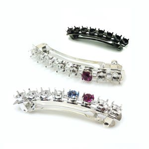 May include: Three silver hair clips with clear rhinestones and colourful gemstones. The clips are curved and have a row of rhinestones along the top. The gemstones are red, blue, and purple.