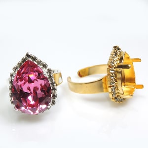 Könnte beinhalten: Zwei Ringe, einer mit einem rosafarbenen, tropfenförmigen Kristall, der in einer silberfarbenen Fassung mit klaren Strasssteinen gefasst ist, und der andere mit einer goldfarbenen Fassung mit klaren Strasssteinen.
