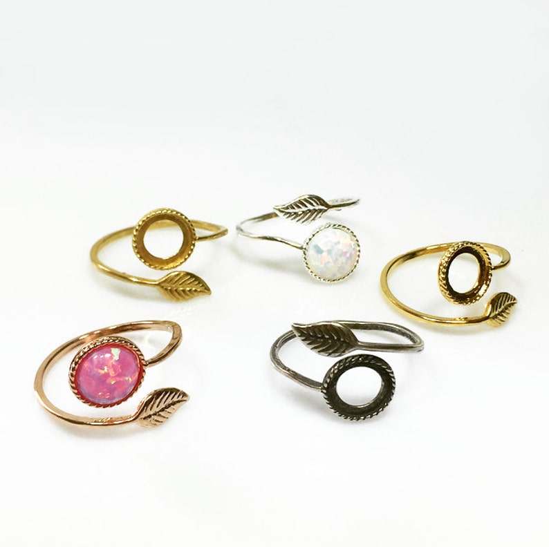 May include: Four adjustable rings with a leaf design. Two rings have a clear bezel setting, one ring has a pink opal stone, and one ring has a white opal stone.