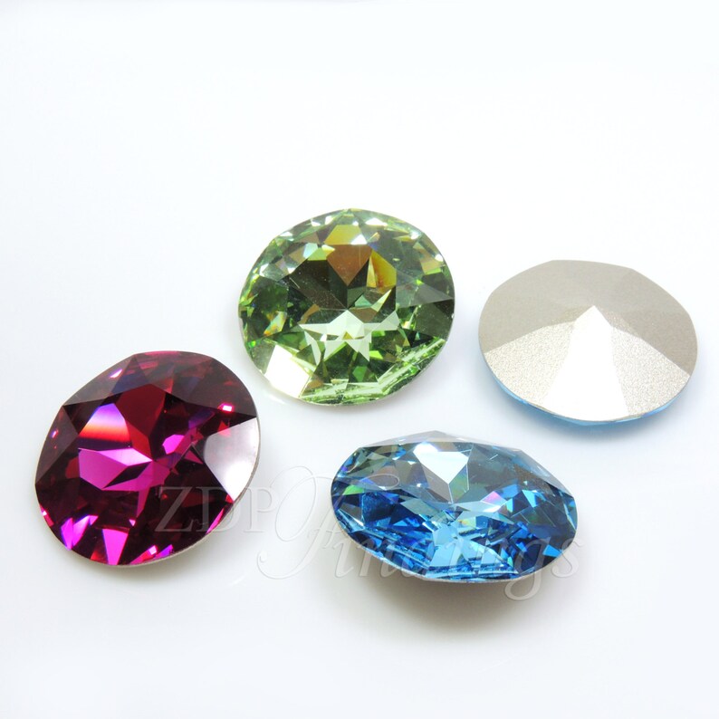 May include: Four faceted gemstones in shades of red-violet, green, blue, and silver. The gemstones are oval and round, with multiple facets to reflect light. The gems are set against a white background.