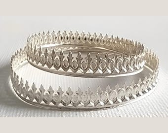 May include: Two silver bangles with a decorative crown-like design. The bangles are stacked on top of each other.