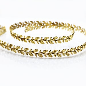 Könnte beinhalten: Zwei goldene, blattartige Haarreifen aus Draht. Die Haarreifen bestehen aus dünnem Draht mit einem zarten Blattdesign.