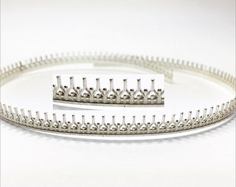 May include: Silver metal trim with a decorative scalloped edge. The trim is in the shape of a circle and has a repeating pattern of small, pointed arches.