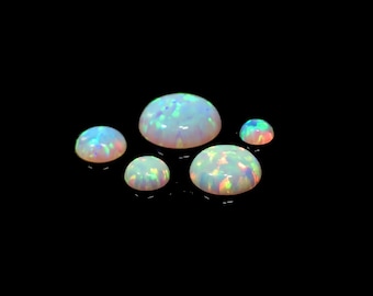 May include: Four iridescent opal cabochons of varying sizes, set against a black background. The opals are white with flashes of blue, green, and pink.