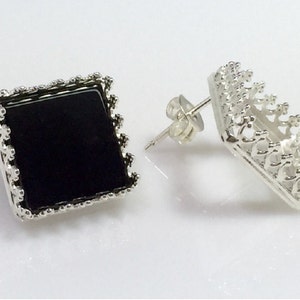 May include: A pair of silver earrings with a square black stone set in a decorative frame. The earrings have a post back closure.