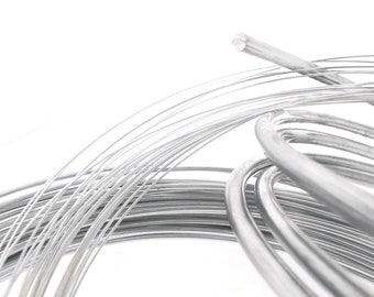 May include: A close-up of a coil of silver wire. The wire is coiled in a spiral shape and is shiny and reflective.