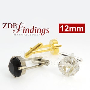 Puede incluir: Tres gemelos con engastes redondos de 12 mm. Un gemelo tiene un cristal negro, otro tiene un cristal transparente y el último está vacío. Los gemelos son plateados con detalles dorados. El texto "ZDP Findings Manufacturer" es visible en la imagen.