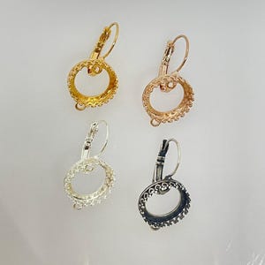May include: Four earring settings in different finishes: gold, rose gold, silver, and black. Each setting features a round bezel with a decorative edge and a loop for attaching a pendant.