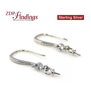 May include: Two sterling silver earring hooks with a small, clear gemstone and a decorative beaded design. The hooks are curved and have a loop for attaching additional charms or beads. The text "Sterling Silver" is visible.