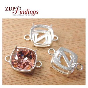 Puede incluir: Tres engastes de metal plateados para una piedra preciosa de forma cuadrada. Los engastes tienen un pequeño bucle a cada lado. El engaste central tiene una piedra preciosa rosa claro. El texto "ZDP Findings Manufacturer" es visible en la esquina superior izquierda de la imagen.