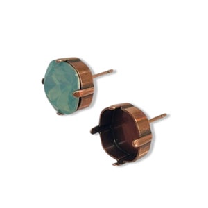 May include: A pair of copper earring settings with a light green opal stone in one setting. The settings are designed to hold a round stone.