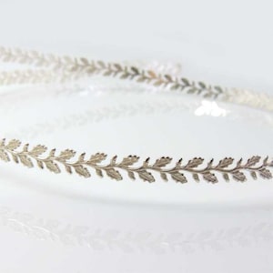 May include: A silver headband with a delicate leaf design. The headband is thin and flexible, making it comfortable to wear.
