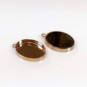 May include: Two gold-toned oval-shaped metal pendant trays with a loop at the top for attaching a chain or cord.