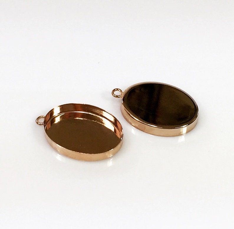 May include: Two gold-toned oval-shaped metal pendant trays with a loop at the top for attaching a chain or cord.
