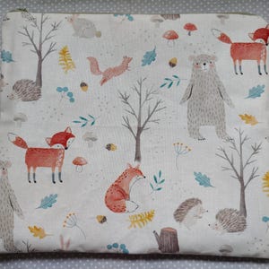 May include: A white fabric pouch with a woodland animal print. The print features foxes, bears, hedgehogs, and trees. The pouch is ideal for storing small items.
