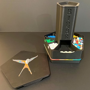 May include: A black plastic candy dispenser with the word "BIRBS" printed on the side. The dispenser has multiple compartments filled with colourful sweets and a lid with a bird graphic.