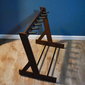 May include: A dark brown wooden guitar stand with a unique angled design. The stand features multiple horizontal bars for holding guitars and a sturdy base. The stand is made of wood and has a natural finish.