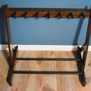 May include: A mid-century modern coat rack made of dark wood with six hooks. The rack has a rectangular frame with a horizontal bar at the bottom for storage. The design is minimalist and functional, suitable for entryways or bedrooms.