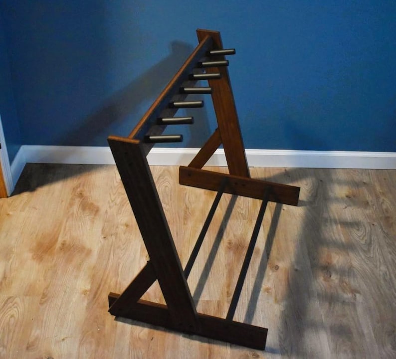 May include: A dark brown wooden guitar stand with a unique angled design. The stand features multiple horizontal bars for holding guitars and a sturdy base. The stand is made of wood and has a natural finish.