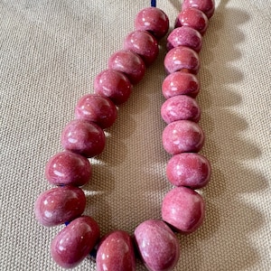 May include: A necklace featuring large, oval-shaped beads in shades of pink and red. The beads are strung on a dark blue cord, creating a striking contrast. The beads have a glossy finish and a marbled appearance.